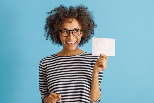 Cheerful woman with gift card standing in studio
