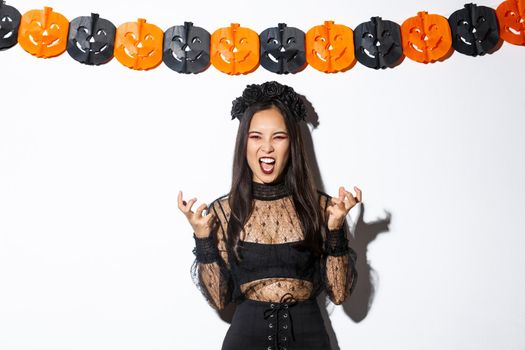 Image of wicked witch laughing evil and grimacing, woman celebrating halloween against party decorations, standing over pumpkin streamers