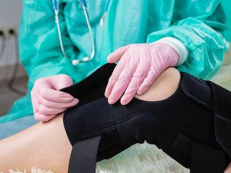 Physiotherapist helps a woman put on a brace after leg surgery. Close-up of a doctor's hand