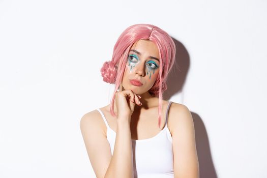 Close-up of nostalgic sad girl in pink wig, looking left thoughtful, standing over white background