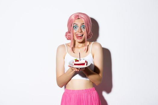 Portrait of cute girl licking lips as holding delicious cake, celebrating birthday, wearing pink wig and bright costume for party