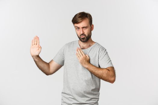 Funny bearded man in gray t-shirt, showing martial arts skills and pouting, standing over white background