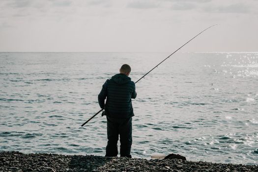 Man hobby fishing on sea tightens a fishing line reel of fish. Calm surface sea. Close-up of a fisherman hands twist reel with fishing line on a rod. Fishing in the blue sea outdoors.
