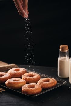 Baker pours sugar over pastry on a bakery tray 