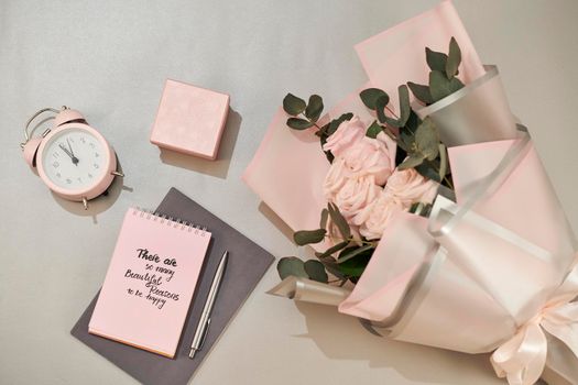 Gift box, alarm clock and pink rose flowers on white table top view in flat lay style. Greeting card for Mother or Woman day.