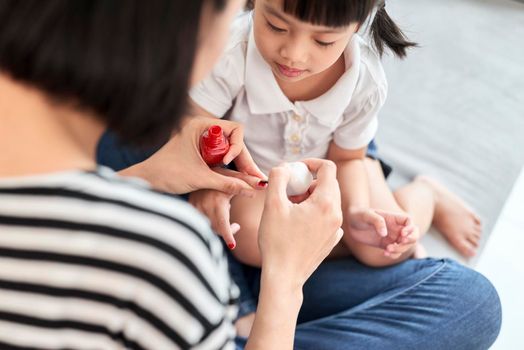 Beautiful young mother is painting the nail varnish to her cute little daughter