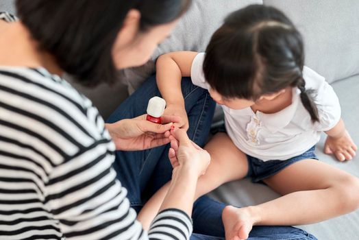 Beautiful young mother is painting the nail varnish to her cute little daughter
