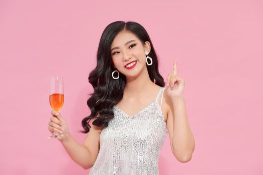 Cute girl with shiny skin holding wineglass and standing in elegant pose on beige background. 