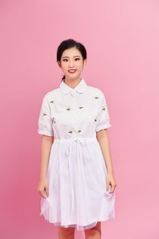 Cute and attractive asian woman standing in modest smiling at camera while standing over pink background.
