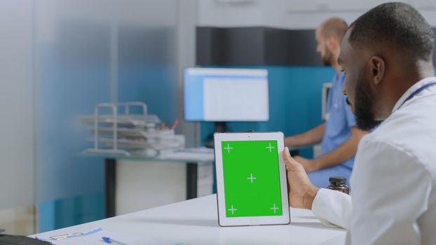 Medical team analyzing sickness expertise working at healthcare treatment in hospital office. African american therapist doctor holding mock up green screen chroma key tablet with isolated display