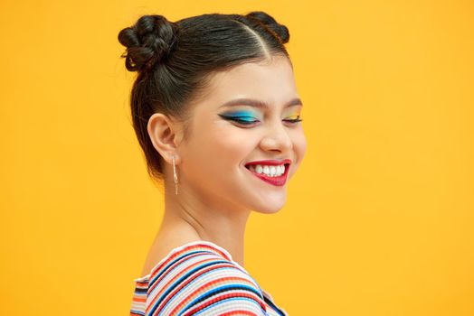 Cheerful woman with appealing smile, having hair bun wearing isolated over yellow background. 