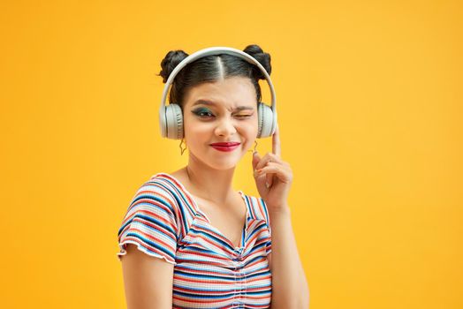 Young lady with buns hair and listening to music with headphones on yellow background