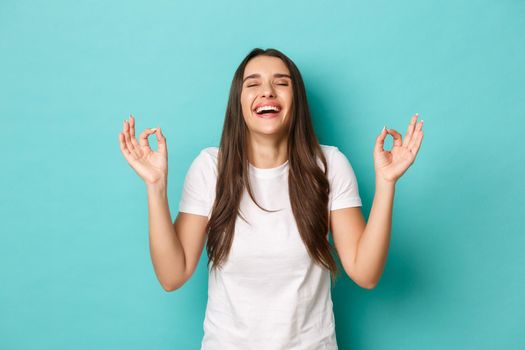 Image of satisfied female in white t-shirt, laughing and showing okay signs in approval, like and agree with something good, standing over blue background