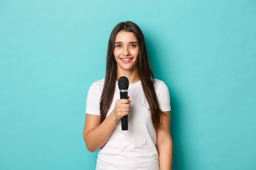 Image of young happy woman in white t-shirt, giving a speech, holding microphone to sing or perform, standing over blue background