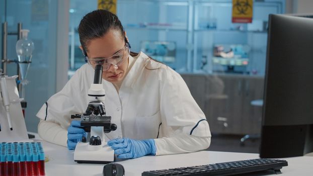 Specialist with safety goggles using microscope in laboratory