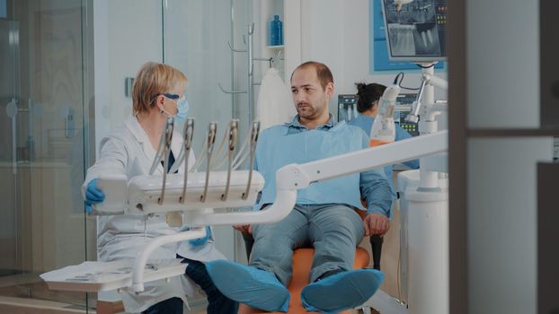 Stomatologist doing dental examination with orthodontic tools and instruments, treating patient with toothache. Dentist using drill and dentistry equipment at oral care examination.