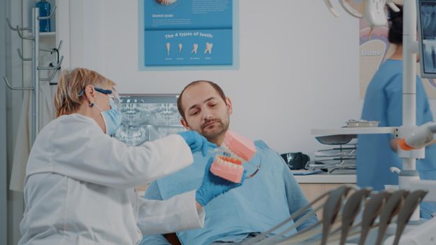 Stomatologist using artificial jaw to explain correct way to brush teeth