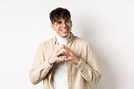 Portrait of hipster guy in glasses with white smile, steeple fingers as having plan, scheming something interesting, standing cunning on white background