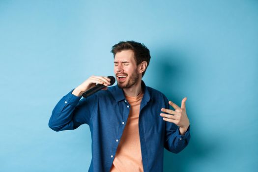 Romantic guy singing song in microphone and gesture, singer playing karaoke, standing on blue background