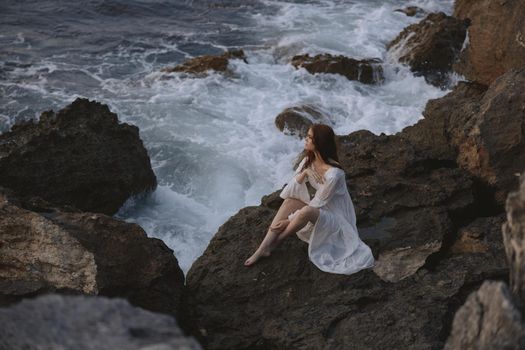 pretty woman with wet hair in white dress sits on waves stones. High quality photo