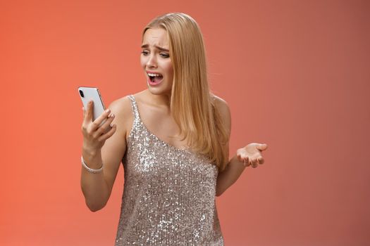 Troubled concerned arrogant young blond woman complaining yelling smartphone cannot call friend no signal holding smartphone look mobile display pissed moody arguging, red background