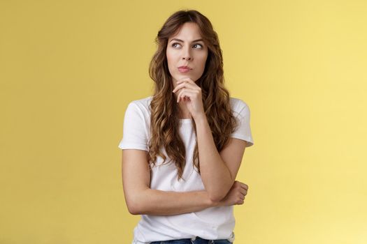 Thoughtful smart creative female freelancer trying solve puzzle making choice pondering decision touch chin thinking look away focused thinking deep stand yellow background