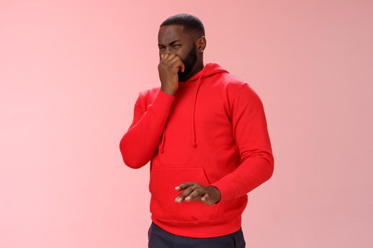 Intense bothered african american man feel unwell close nose cringe dislike aversion wanna puke smell terrible reek, disgusting stink, expressing disgust look junk, standing pink background