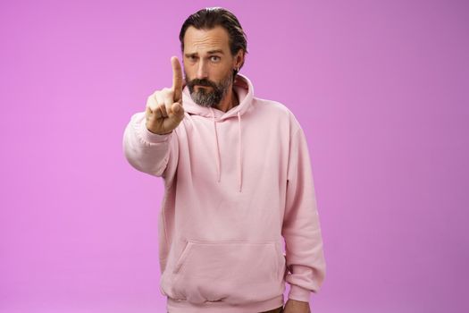 One rule listen. Serious-looking bossy focused determined adult bearded male in pink hoodie extend index finger first number scolding making statement forbid bad behaviour, purple background