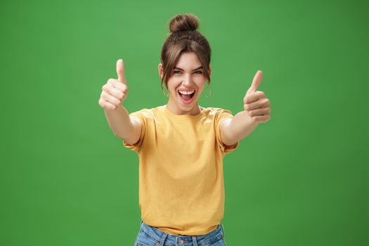 Portrait of cheerful enthusiastic and excited emotive beautiful european woman in yellow t-shirt pulling hands with thumbs up towards camera smiling broadly, being supportive, liking idea