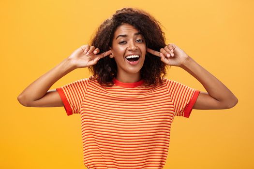 Do not care what saying cannot hear you. Carefree indifferent good-looking african american woman with curly hairstyle closing ears with index finger singing lalala during argument behaving childish