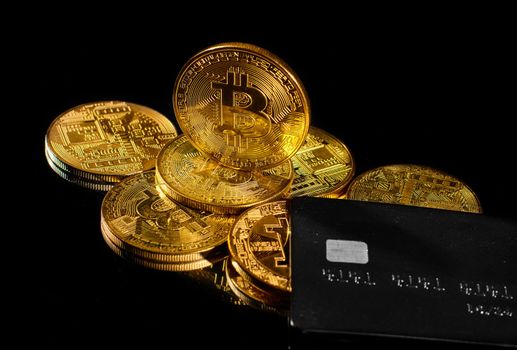 Golden coin with bitcoin logo and credit card. Leader in cryptocurrency BTC and bitcoin rewards card against black surface. Decentralized digital currency. Crypto payment. Electronic money or e-cash