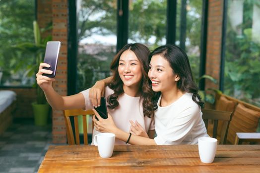 Two young and attractive females taking selfie while sitting in the cafe.