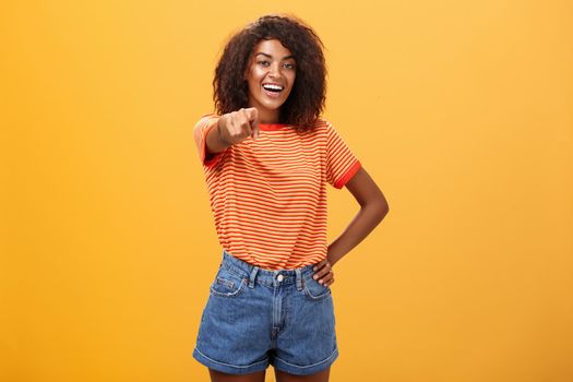 We hire you. Confident happy and awesome dark-skinned fashionable woman with curly hair holding hand on waist pointing at camera with index finger as if picking person or candidate, smiling