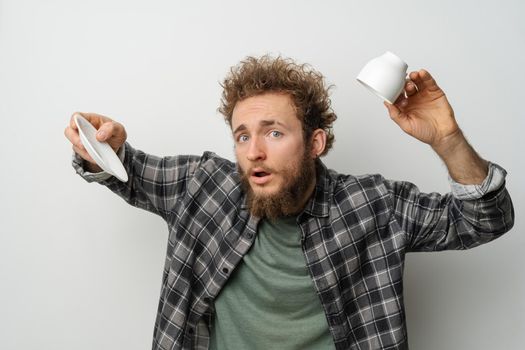 No coffee in inverted cup good looking man with curly hair and beard holding cup, wearing plaid long sleeve shirt isolated on white background. Crisis and lockdown concept