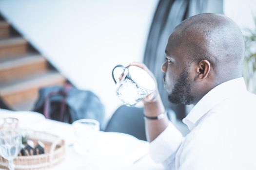 Young Man in a White Shirt Sits Back to the Camera and Holds a Cup of Coffee or Tea in his Hand. Snack Time. Close-up