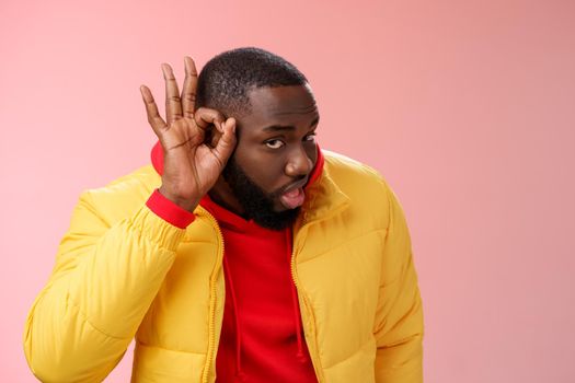 Curious funny charismatic black bearded guy bending forward hold hands ear eavesdropping wanna overhear girlfriend conversation behind door standing curious gossiping pink background