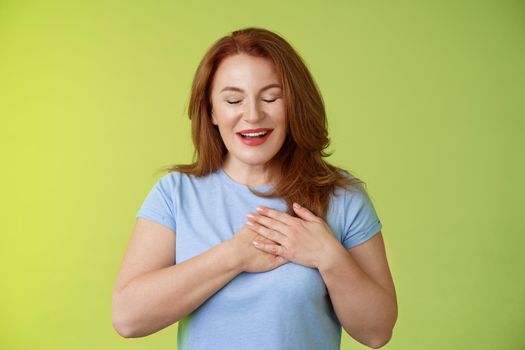 Fascinated cute redhead passionate middle-aged woman sighing lovely touch heart close eyes smiling delighted express admiration temptation feeling appreciation grateful emotions green background