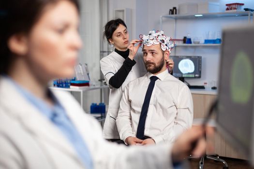 Specialist woman in neuroscience adjusting eeg headset analyzing brain activity of man