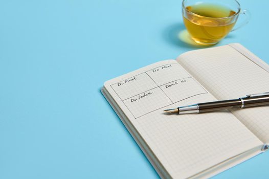 Time management, deadline concept: An open organizer notebook with timetable of the day by hour, ink pen, a tea cup on color background, copy space. Cropped image