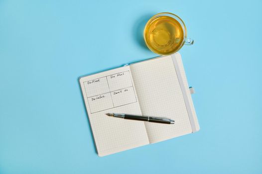 Time management, deadline concept: Flat lay of an open organizer notebook with timetable of the day by hour, ink pen, a tea cup on color background, copy space. Cropped image