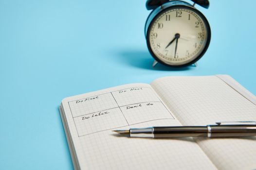 Time management, deadline concept: An open organizer notebook with timetable of the day by hour, ink pen, alarm clock on color background, copy space. Cropped image