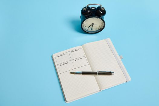 Time management, deadline and concept of proper planning and organization of time: An open organizer notebook with timetable of the day by hour, ink pen, alarm clock on colored background, copy space.