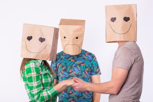 Love triangle, jealousy and unrequited love concept - woman and man with bags over heads holding hands and another man is angry.