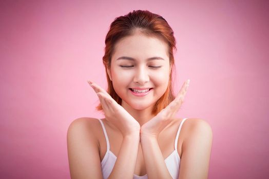 Portrait of attractive Vietnamese woman touching her face on pink background.