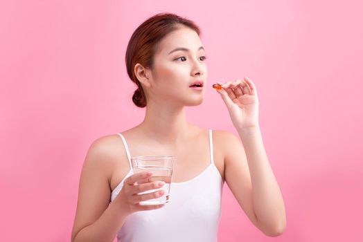 Young asian beauty young woman eating pills and drinking water on pink background.