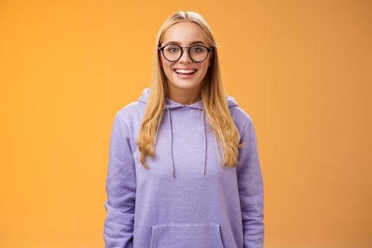 Charming female student geek smiling energized wanna participate university event grinning look excited wearing glasses purple hoodie standing amused orange background having fun