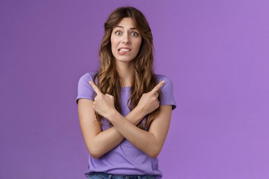 Perplexed timid hesitant worried girlfriend afraid making bad choice cross hands pointing sideways indicating left right perplexed decide frowning pull hesitant face asking advice purple background