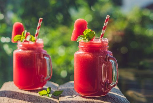 Healthy watermelon smoothie in Mason jars with mint and striped straws against the background of greenery