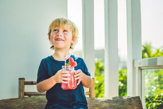 The boy is holding Healthy watermelon smoothie in Mason jar with mint and striped straws on a wood background