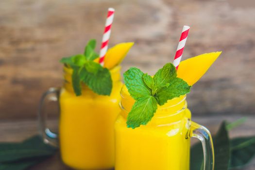 Juicy smoothie from mango in two glass mason jars with striped red straw on old wooden background. Healthy life concept, copy space